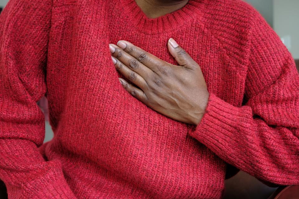 A person wearing a textured sweater places a hand on their chest in a gesture of affection or pledge