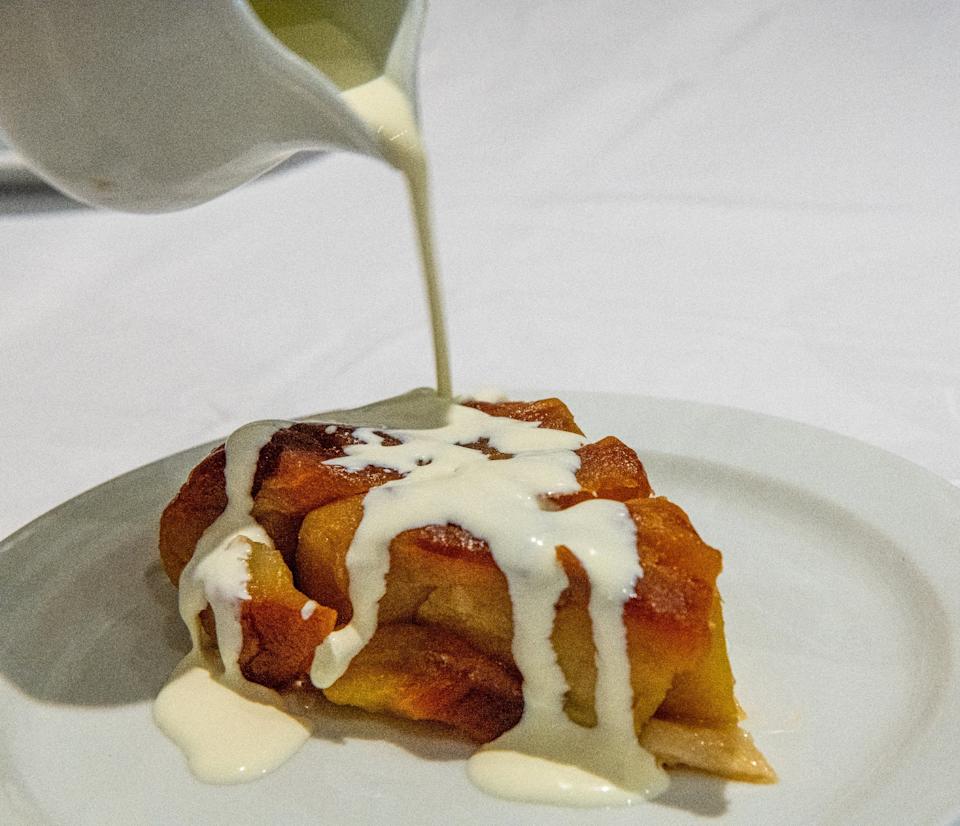 Pouring cream over a slice of dessert bread pudding on a white plate