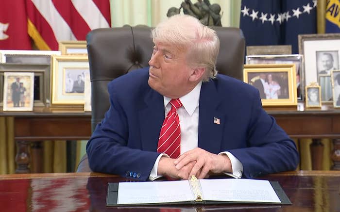 Man in a suit sits at a desk, looking sideways, with family photos in the background