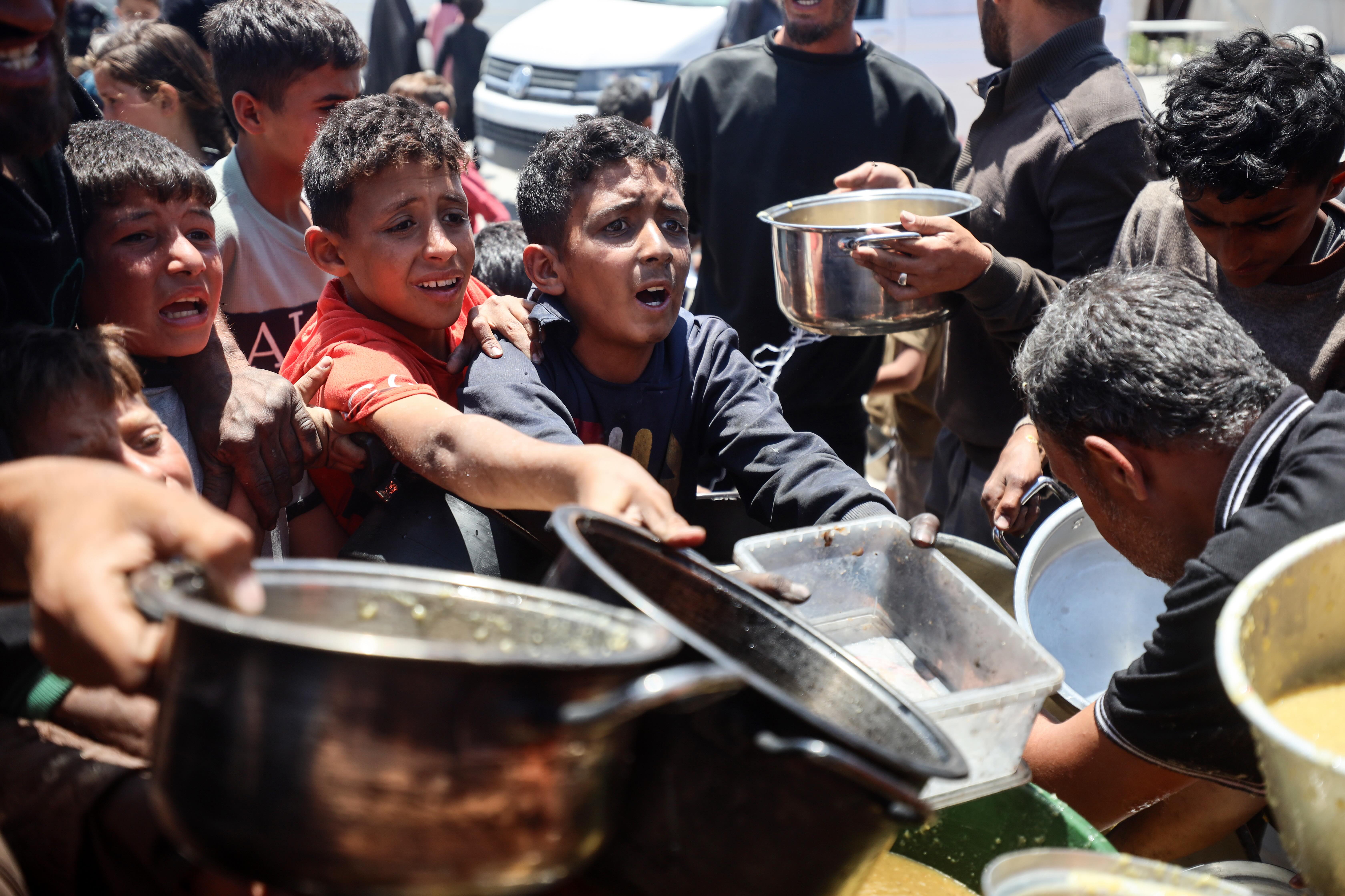 Palestinian youths try to get a ration of hot food from a charity kitchen set up at a camp for displaced people in Gaza City, on May 21, 2025.