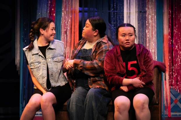Three actresses sit, two facing each other, the third looking at the audience.