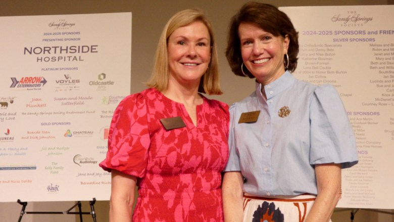 New Sandy Springs Society President Sana Thomas and outgoing President Beth Robertson stand in front of lists of sponsors during the annual meeting. (Photo by Bob Pepalis)