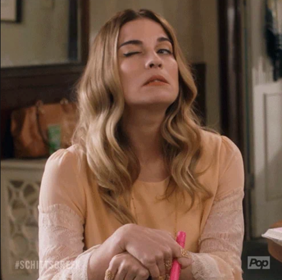 Person with wavy hair in a lacy top making a playful, exaggerated wink, holding a pink marker