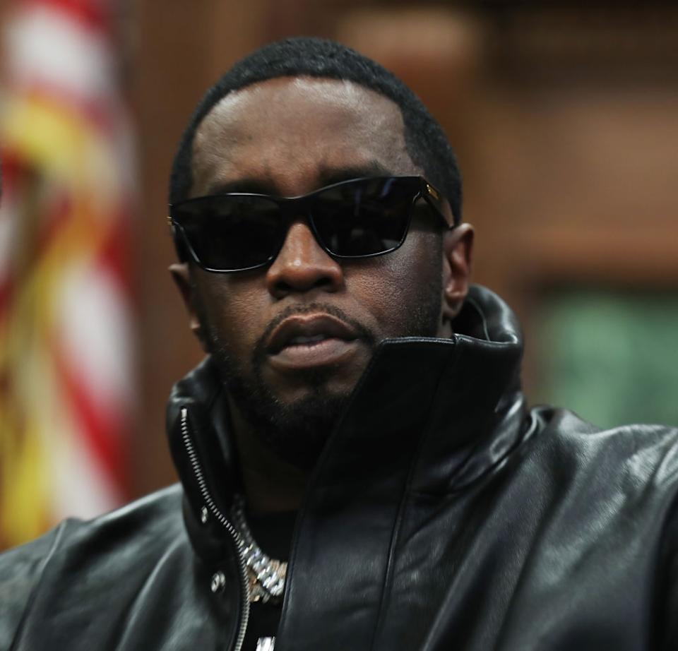 Person in sunglasses and a sleek leather jacket gazes forward confidently. Background is blurry and out of focus