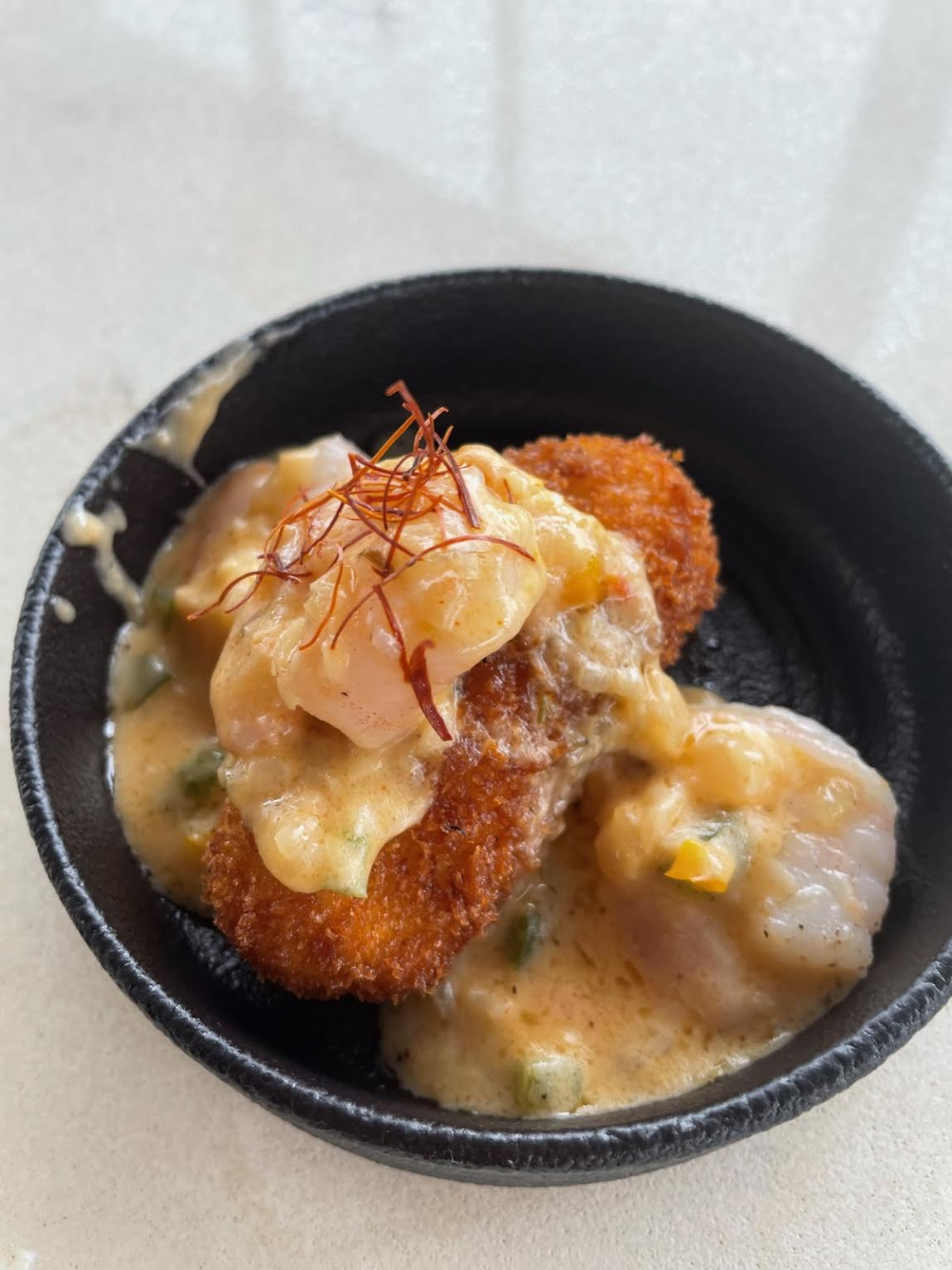 A black bowl containing breaded shrimp with creamy grits from peckish in Atlanta.
